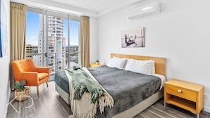 Une chambre d’hôtel moderne, dotée d’un grand lit, d’une chaise, d’une table de chevet et offrant une vue sur le paysage urbain grâce à de grandes fenêtres.