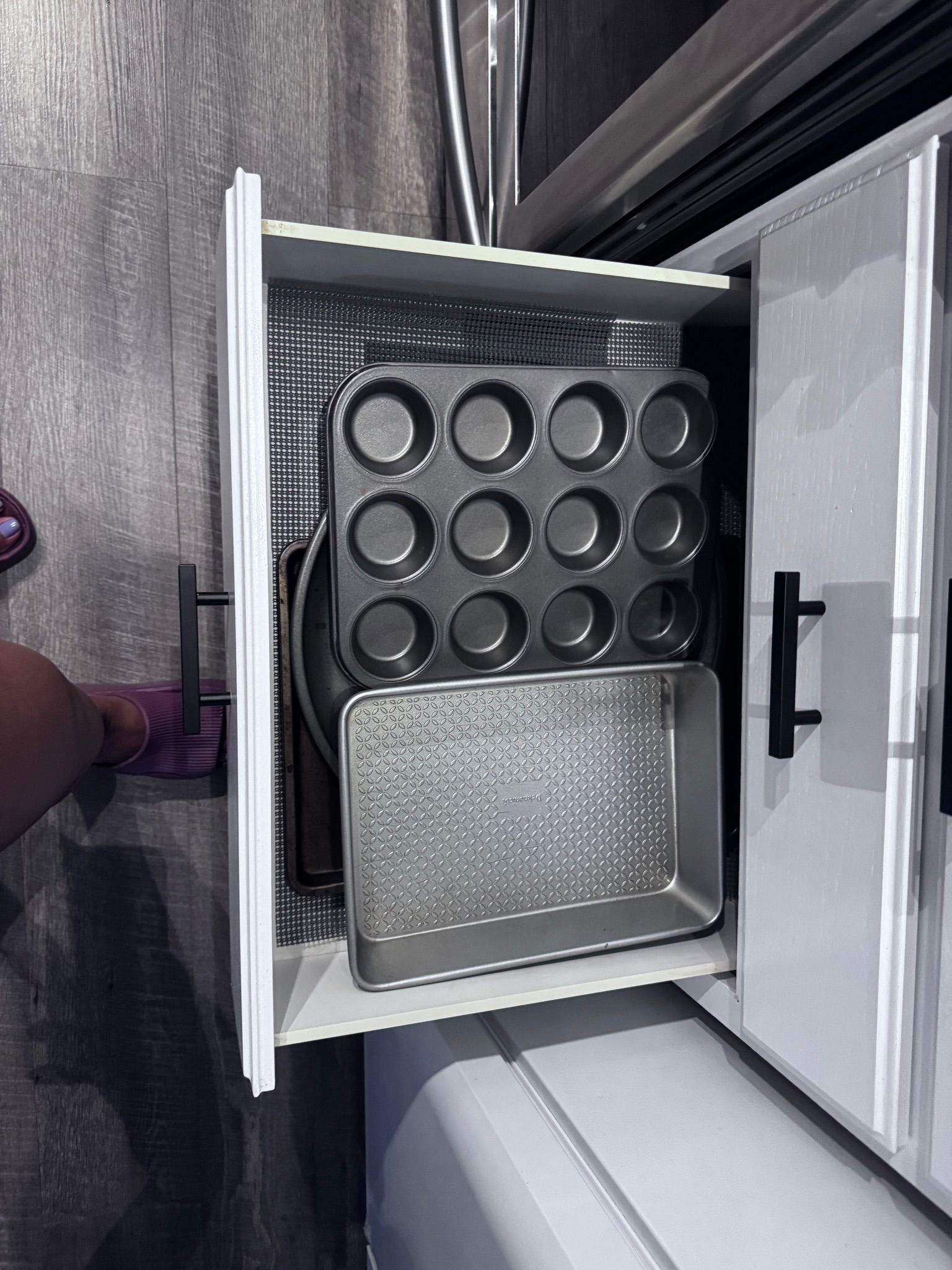 A kitchen cabinet with a muffin tray and a baking tray inside.