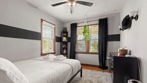 Ein Schlafzimmer mit Bett, Deckenventilator, Kommode und einem Fenster mit Vorhängen.
