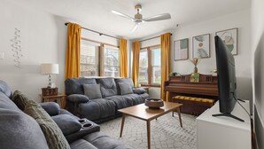Ein Wohnzimmer mit einer Couch, einem Couchtisch, einem Fernseher, einem Klavier und gelben Vorhängen.