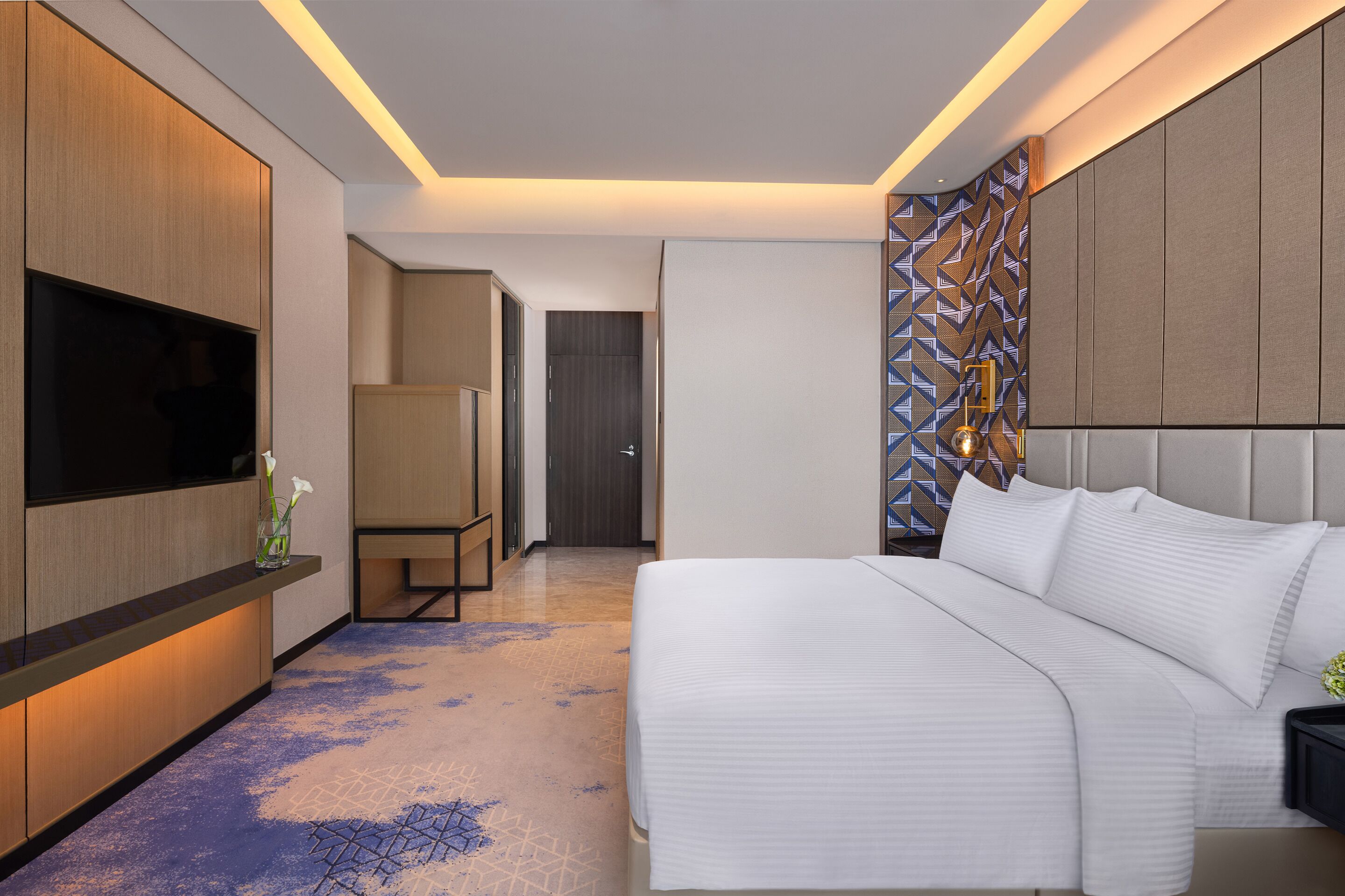 A modern hotel room with a large bed, a flat-screen TV, a desk, and a patterned wall.