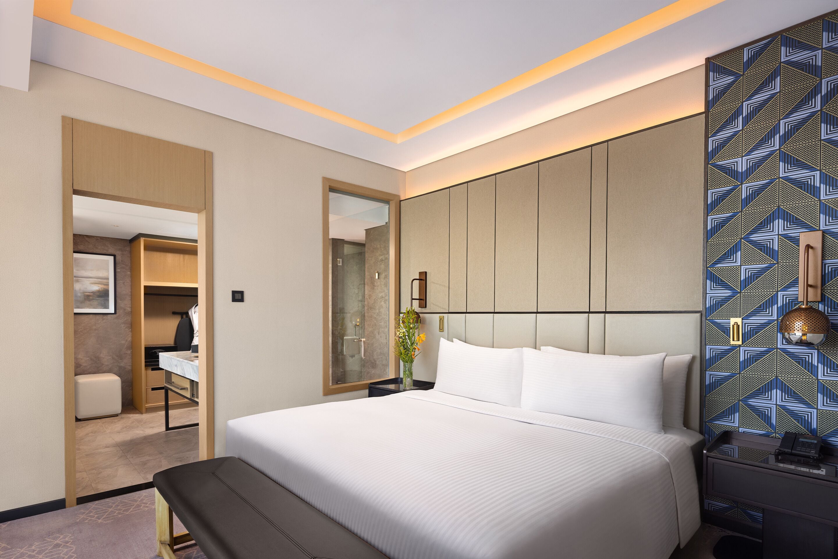 Une chambre d’hôtel moderne avec un grand lit, une table de chevet, un miroir et un mur décoré d’un motif.
