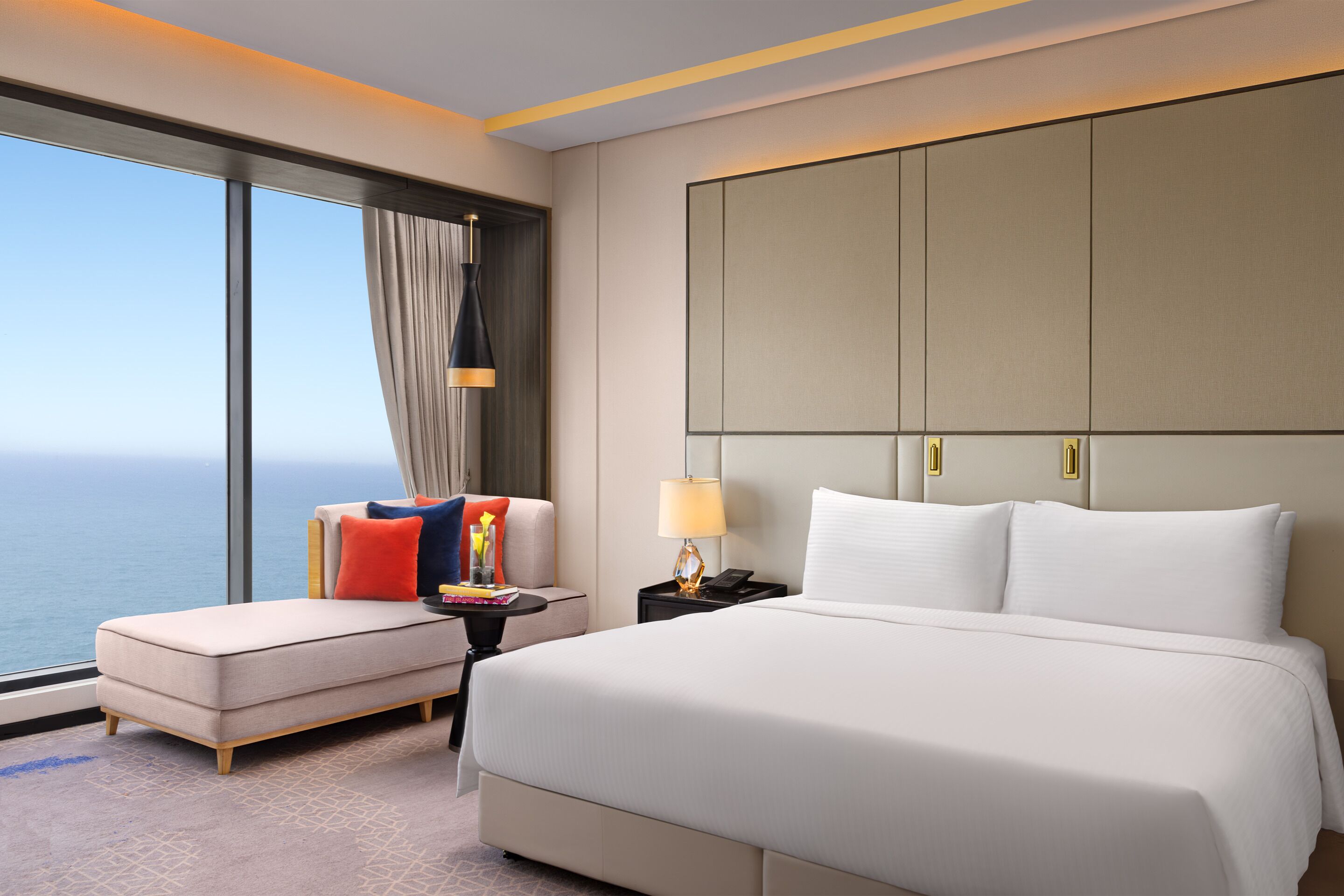 A hotel room with a large bed, a seating area, a nightstand, a lamp, and a view of the ocean.