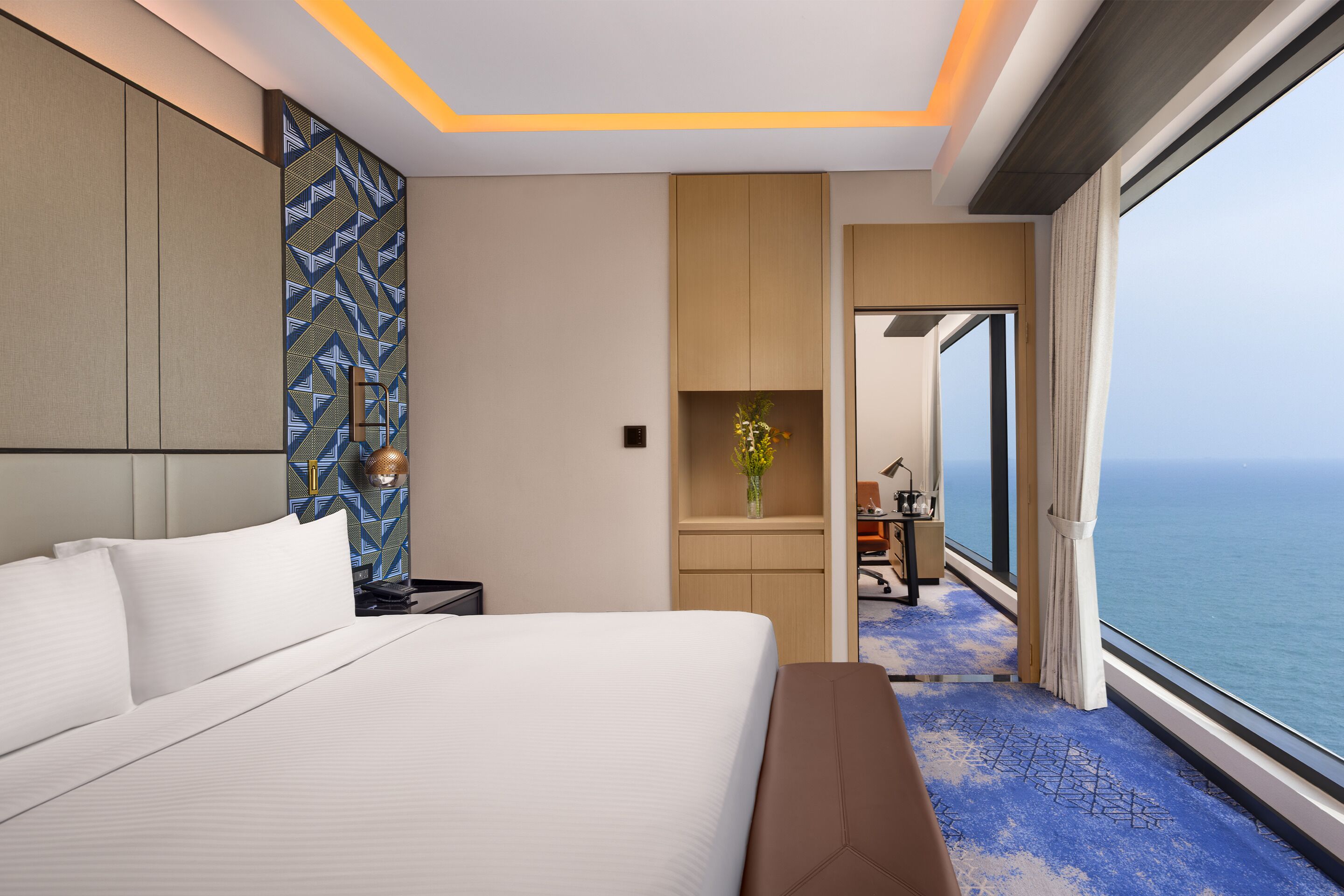 Habitación de hotel moderna con una cama grande, un escritorio y vista al océano.