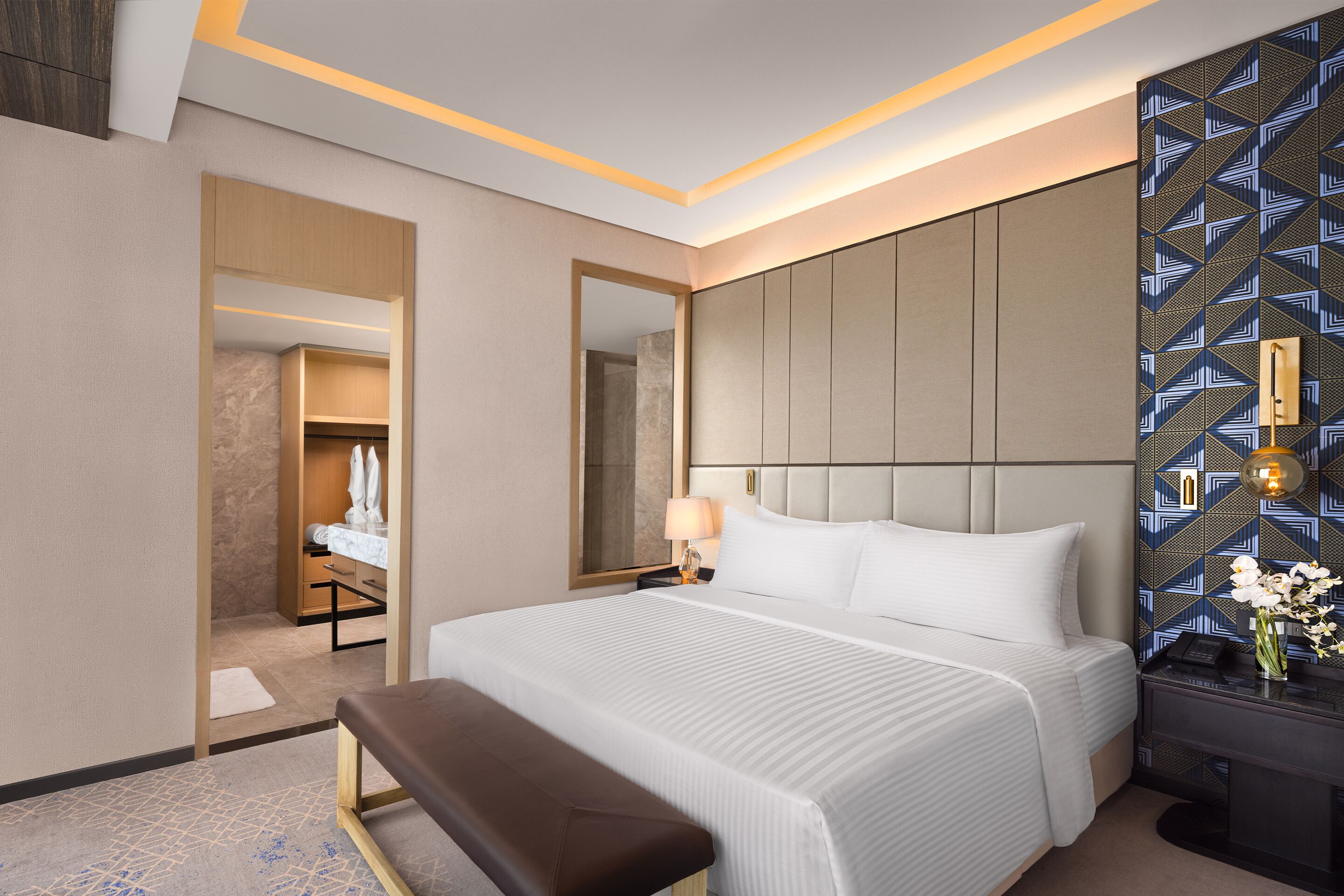 Una habitación de hotel moderna con una cama grande, un banco, una mesita de noche y un espejo.