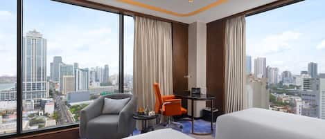 Ein Hotelzimmer mit weitreichendem Stadtblick, einem Bett, einem grauen Sessel, einem orangefarbenen Stuhl und einem kleinen Tisch mit Lampe.