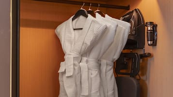 A hotel room with a wooden wardrobe, a black chair, and a white robe hanging on the door.