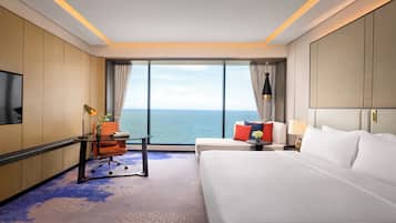 Habitación de hotel con una cama grande, un escritorio con silla, televisor y vista al mar.