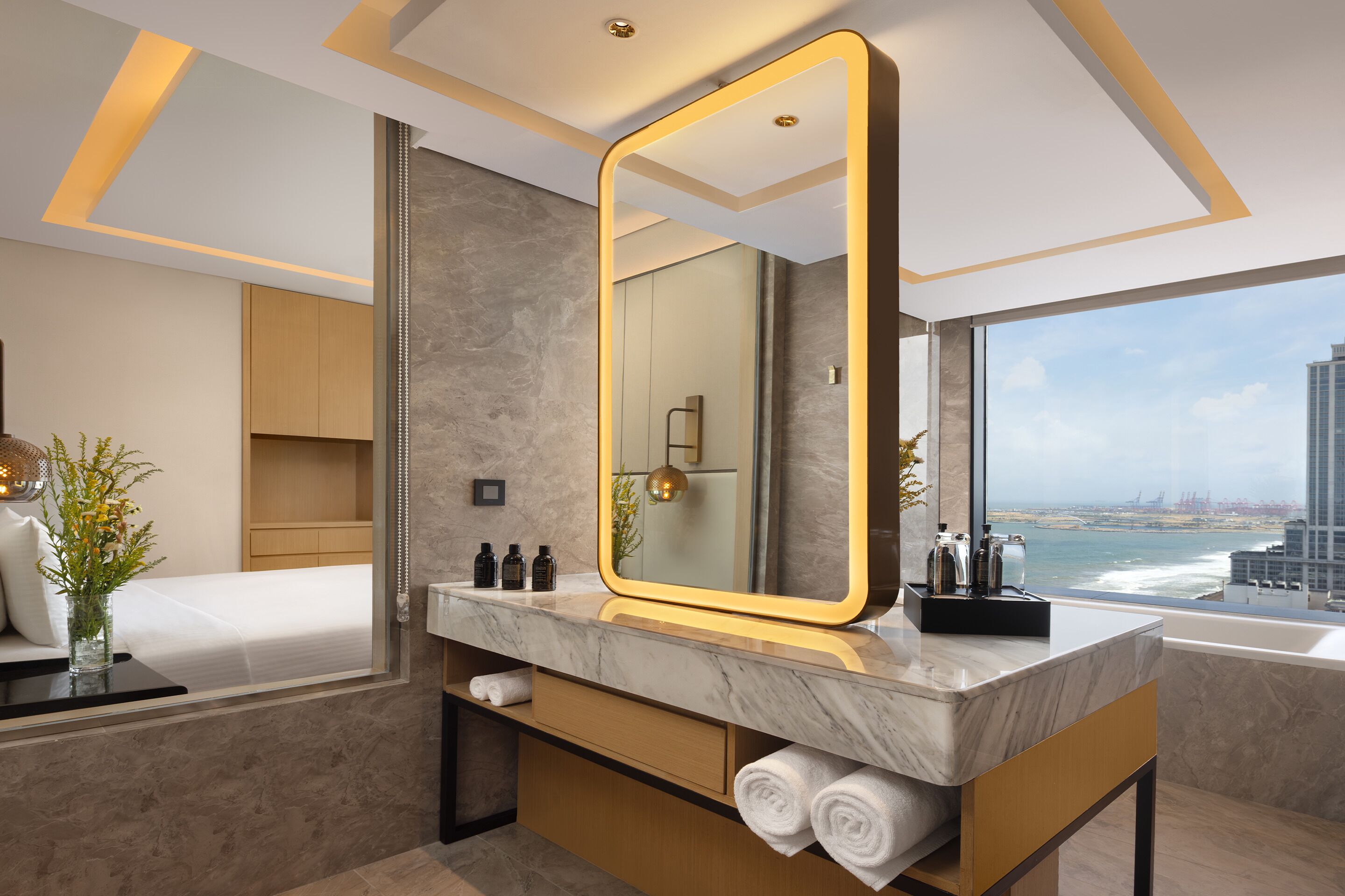 A modern bathroom with a large mirror, marble countertop, and a view of the ocean.