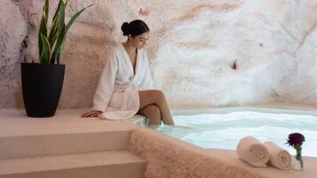 A person in a bathrobe sitting by a stone wall, with a potted plant and towels on the steps.