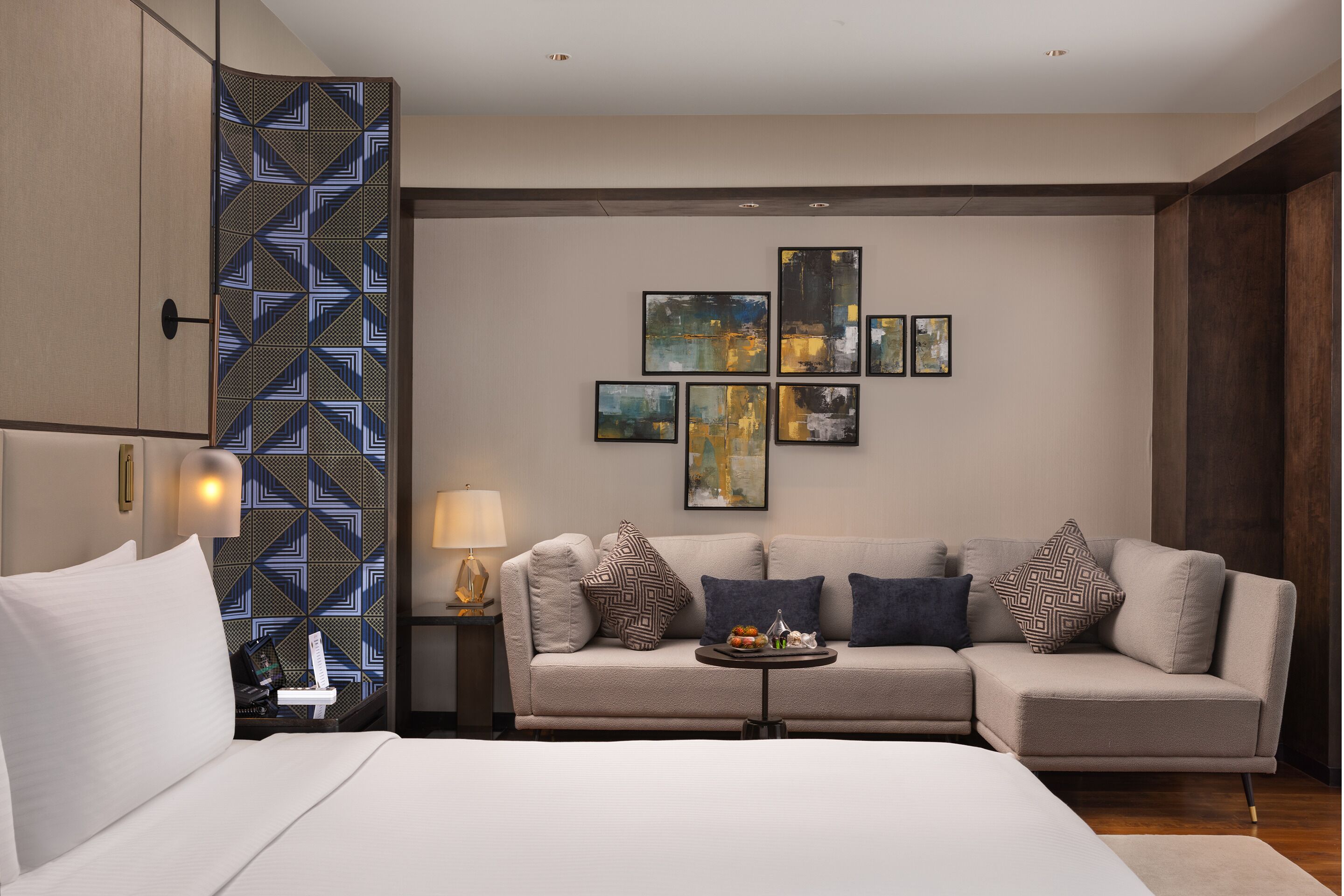 Et moderne hotelværelse med seng, sofa, et natbord med lampe og billedkunst på væggen.