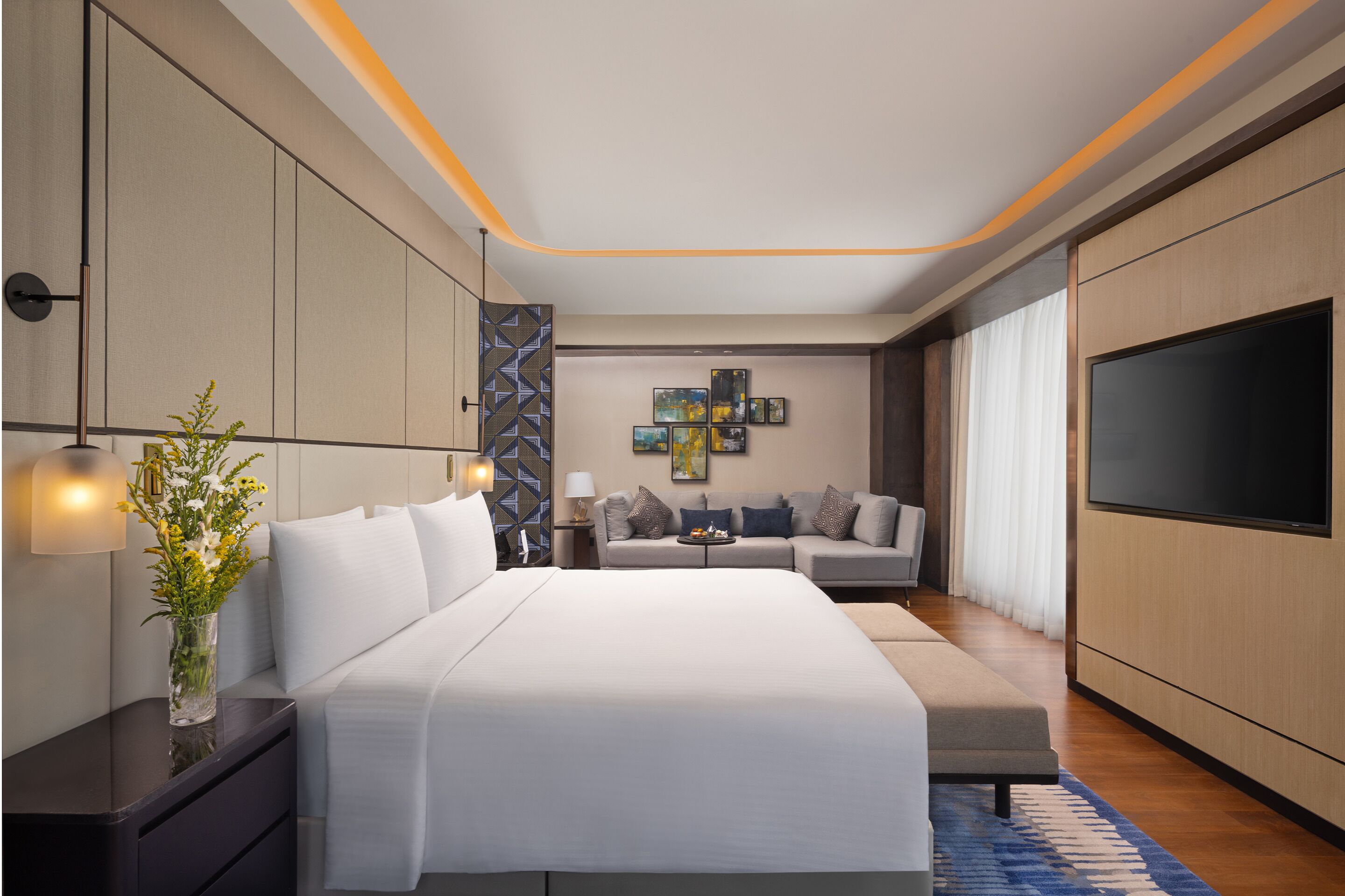 Une chambre à coucher moderne avec un grand lit, un canapé, une télévision et des œuvres d’art accrochées au mur.