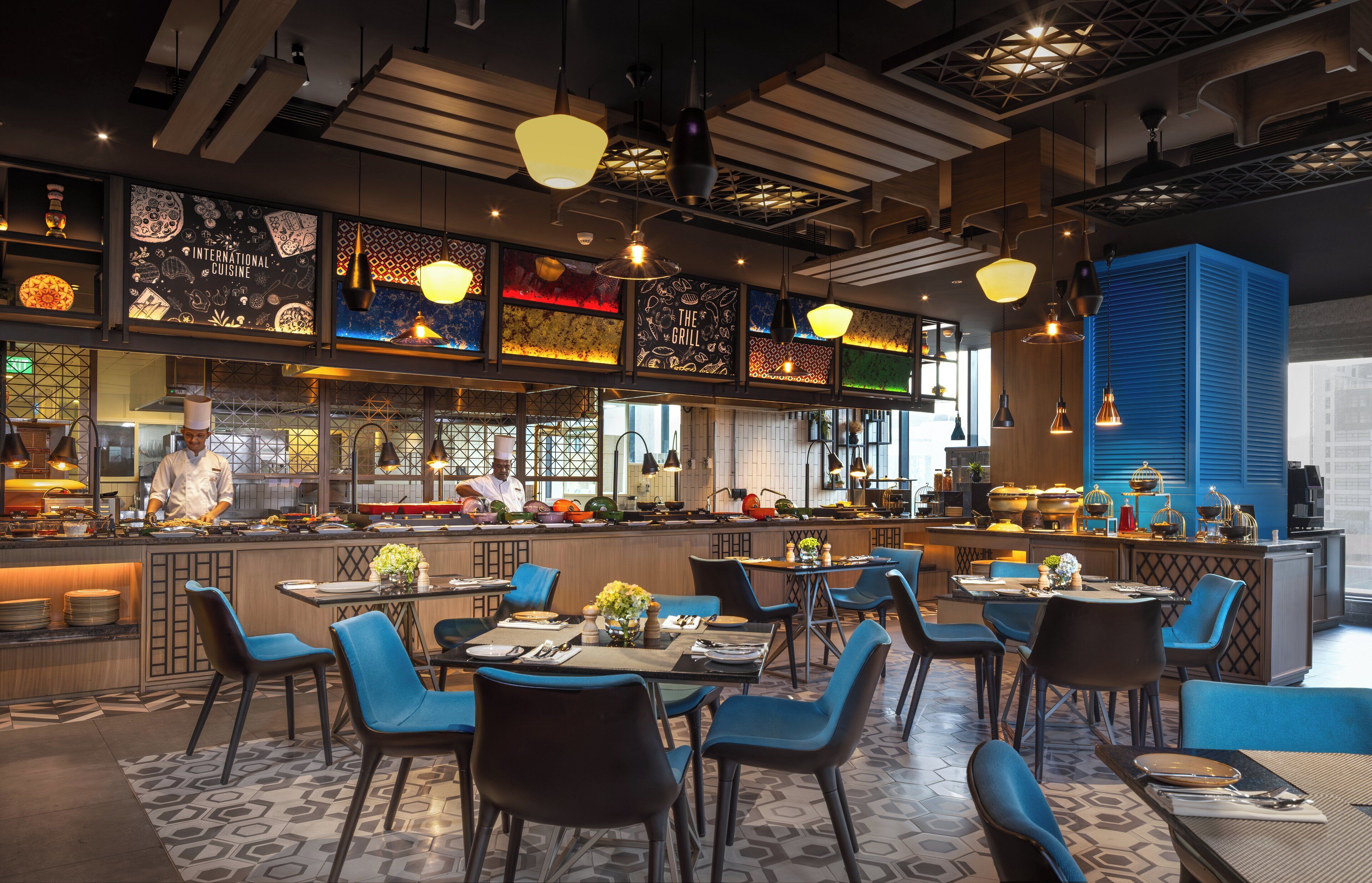 Et moderne restaurantinteriør med barområde, blå stole og et mønstret gulv.