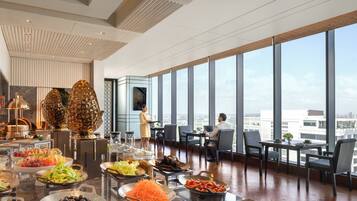 A high-rise hotel room with a panoramic city view, a buffet with various food items, and a modern interior design.