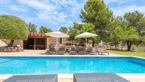 A swimming pool with lounge chairs and umbrellas, a stone building, and trees in the background. - Can Raull in Cales de Mallorca (Manacor)