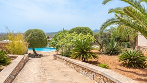 A stone pathway leading to a swimming pool surrounded by various plants and a view of distant hills. - Can Raull in Cales de Mallorca (Manacor)