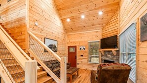 Ein Holzblockhaus-Interieur mit Treppe, Kamin und einer gepolsterten Sitzecke.