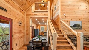 Ein Interieur einer Holzhütte mit Essbereich, einer Treppe und Blick ins Freie.