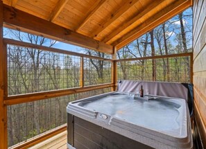 A hot tub in a wooden cabin with a view of trees through large windows. - Smoky Mountain Time (Sevierville)