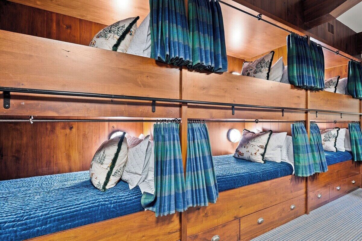Une chambre avec un lit superposé, une tête de lit en bois, un matelas matelassé bleu et un rideau à carreaux.