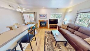 A modern living room with a sofa, TV, fireplace, dining area, and large windows. - Fairway Foothills - 3335 (Moab)