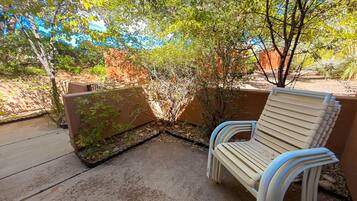 An outdoor seating area with a bench and a concrete floor, surrounded by vegetation and a wall.