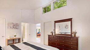 A bedroom with a large bed, a wooden dresser, a mirror, and a view of the outdoors through a window. - Cozy cabin w/hot tub & wraparound deck (Berkeley Springs)