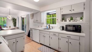 A modern kitchen with white cabinets, a built-in microwave, and a window with a view of greenery. - Cozy cabin w/hot tub & wraparound deck (Berkeley Springs)