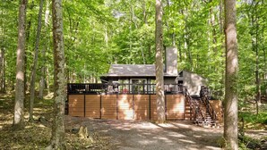 A cabin in a forest with a wooden deck and a chimney. - Cozy cabin w/hot tub & wraparound deck (Berkeley Springs)