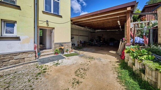 A residential property with a covered outdoor area, a stone wall, and a garden with potted plants.