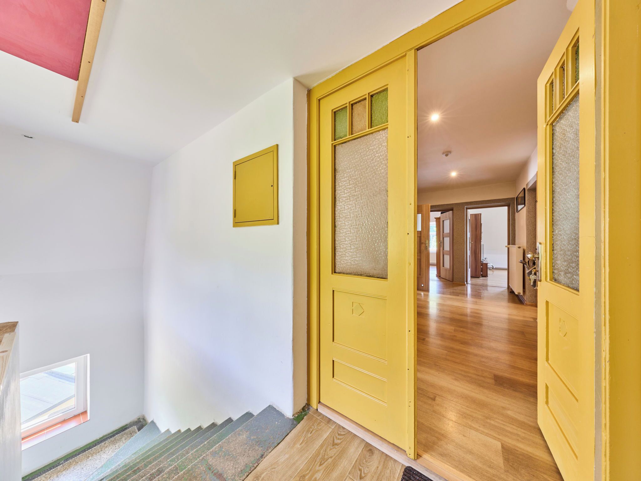 A hallway with a yellow door, a staircase, and a view into another room.