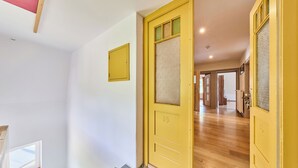 A hallway with a yellow door, a staircase, and a view into another room.