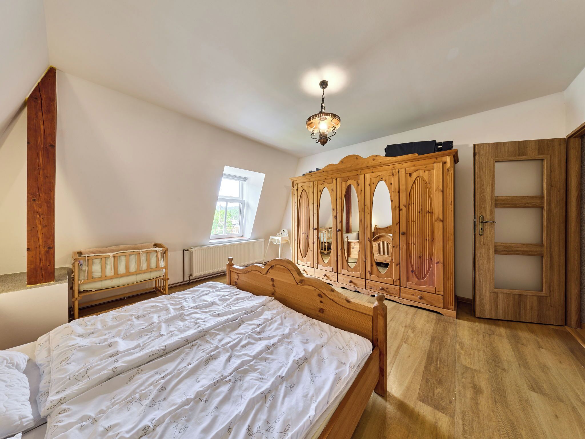 A bedroom with a large bed, wooden wardrobe, and a window.