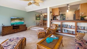 A spacious living room with a television, wicker furniture, a bookshelf, and a ceiling fan. - Manualoha 303 – Ground Floor + PBAC Access (Koloa)