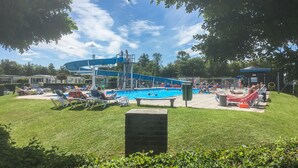 Une piscine avec un toboggan, des chaises longues et une pelouse.