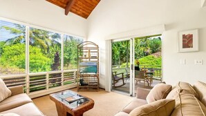 A spacious living area with a large window, a wooden coffee table, and a beige sofa. - Poipu Crater 23 – Vacation in the Crater, AC in Bedrooms (Koloa)