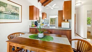 A dining area with a wooden table, chairs, and a ceiling fan. - Poipu Crater 23 – Vacation in the Crater, AC in Bedrooms (Koloa)