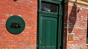 Una puerta verde con un letrero que dice "ARK" sobre un muro de ladrillo.