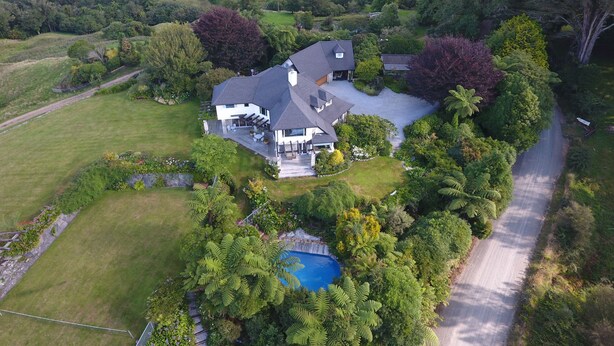 Une grande maison avec une piscine, entourée d’une végétation luxuriante et située dans un paysage vallonné.