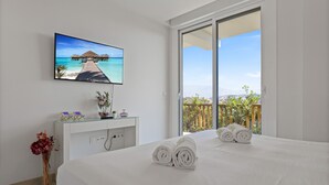 A bedroom with a bed, a TV on the wall, a desk with a vase, and a view of the outdoors. - Golden Horizon | Terrace - pool - sea views (Mijas Costa)