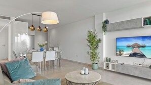 A modern living room with a sofa, coffee table, and TV. There is a dining area with a table and chairs. - Golden Horizon | Terrace - pool - sea views (Mijas Costa)