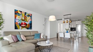 A modern living room with a sofa, a coffee table, and a dining area with chairs and a table. There is a kitchen in the background with a refrigerator and a stove. - Golden Horizon | Terrace - pool - sea views (Mijas Costa)