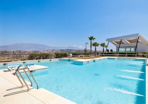 Ein Swimmingpool mit klarem, blauem Wasser, umgeben von Palmen und einem modernen Gebäude mit großen Fenstern.