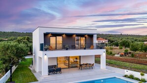 Una casa moderna de dos pisos con balcón, piscina y vistas al paisaje circundante.