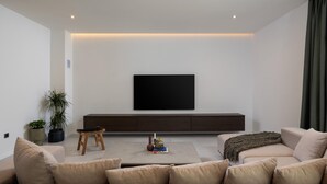 Una sala de estar moderna con un televisor de pantalla plana montado en la pared, un mueble de entretenimiento de madera oscura debajo y dos sofás beige con cojines.