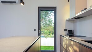 Una cocina moderna con estufa integrada, microondas y pileta. Se ve un ventanal con vista a la vegetación.