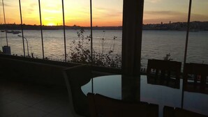 A view from a room with a glass table and chairs, overlooking a river with boats and a sunset. - Cozy 2-bedroom apartment with Stunning Sea Views in enchanting Üsküdar, İstanbul (Üsküdar, İstanbul)