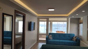 A modern living room with a large window, a blue sofa, and a flat-screen TV. - Cozy 2-bedroom apartment with Stunning Sea Views in enchanting Üsküdar, İstanbul (Üsküdar, İstanbul)