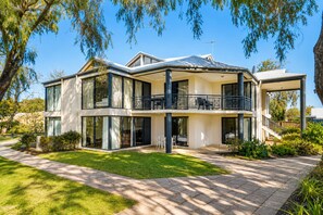 A modern two-story house with large windows, a balcony, and a well-maintained lawn. - 98 Steps To The Beach  (Broadwater)