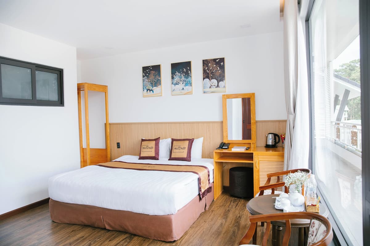 Ett hotellrum med en stor säng, ett skrivbord med en stol, ett fönster med utsikt och konstverk på väggen.